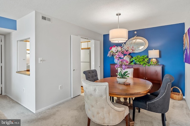 dining room with baseboards, visible vents, light carpet, and a textured ceiling