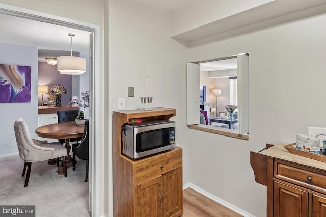 kitchen featuring brown cabinets, electric panel, stainless steel microwave, and baseboards