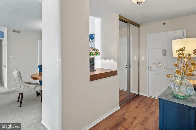 hallway featuring baseboards, visible vents, a textured ceiling, and wood finished floors