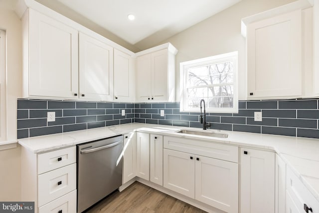 kitchen with a sink, light stone counters, backsplash, and dishwasher