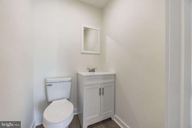 bathroom with toilet, wood finished floors, vanity, and baseboards