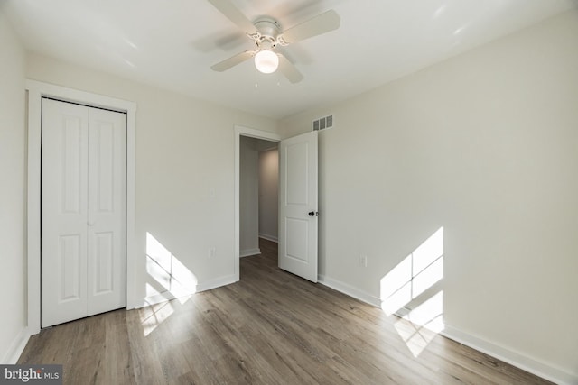 unfurnished bedroom with baseboards, visible vents, ceiling fan, wood finished floors, and a closet