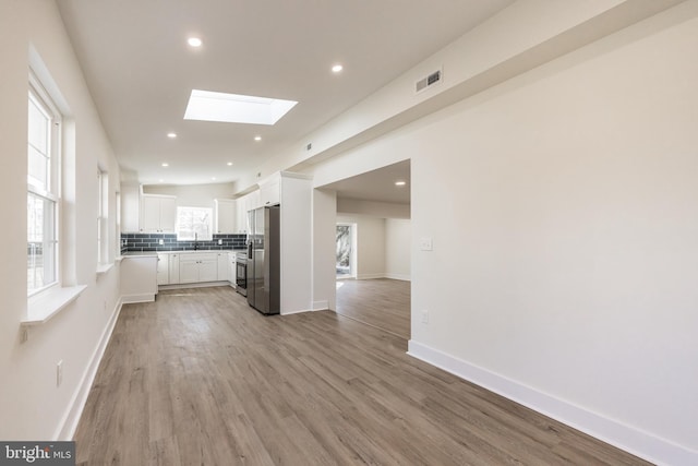 kitchen with a skylight, white cabinetry, visible vents, stainless steel fridge with ice dispenser, and tasteful backsplash