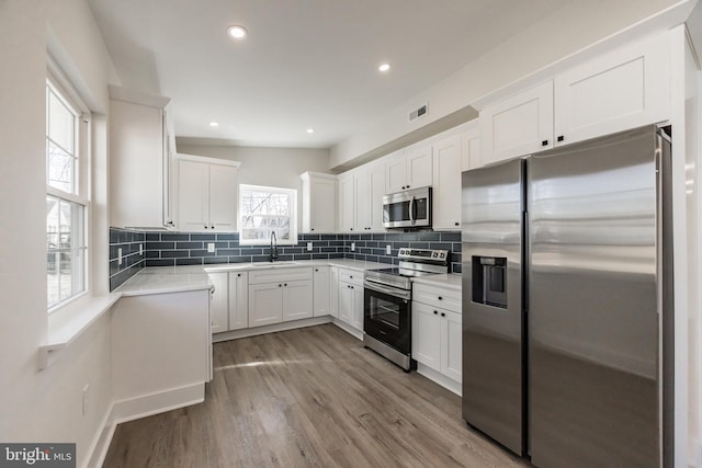 kitchen with stainless steel appliances, light countertops, decorative backsplash, a sink, and wood finished floors