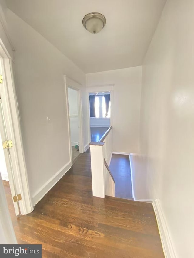 hallway featuring baseboards, dark wood finished floors, and an upstairs landing