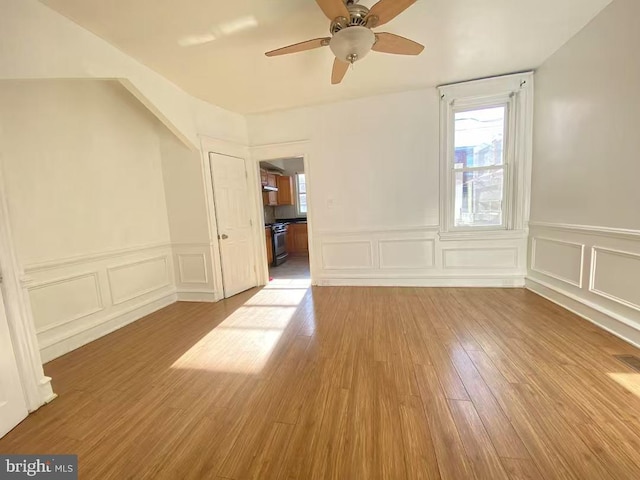 unfurnished room featuring a ceiling fan, a decorative wall, wood finished floors, and wainscoting