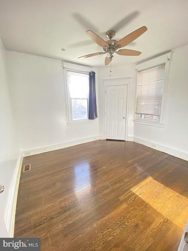 empty room featuring dark wood finished floors, visible vents, and baseboards