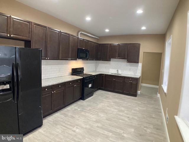 kitchen featuring black appliances, backsplash, dark brown cabinets, and a sink