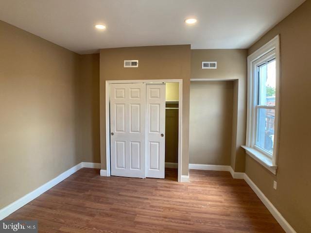 unfurnished bedroom featuring a closet, visible vents, baseboards, and wood finished floors