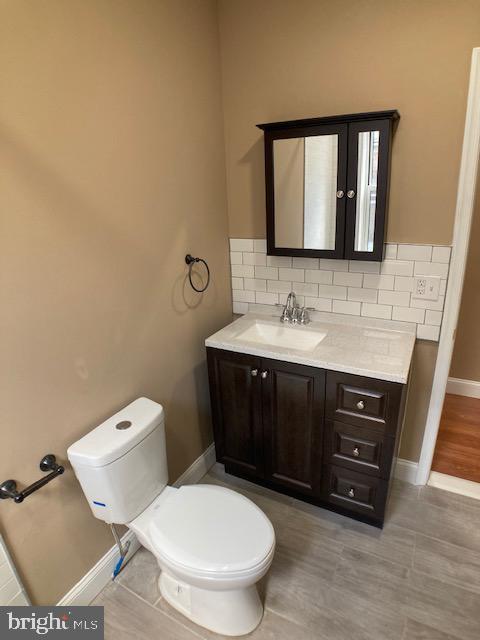 half bathroom with baseboards, toilet, vanity, and decorative backsplash