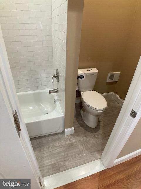 bathroom featuring toilet, visible vents, baseboards, and shower / washtub combination