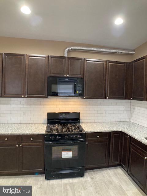 kitchen featuring dark brown cabinetry, black appliances, backsplash, and light stone countertops