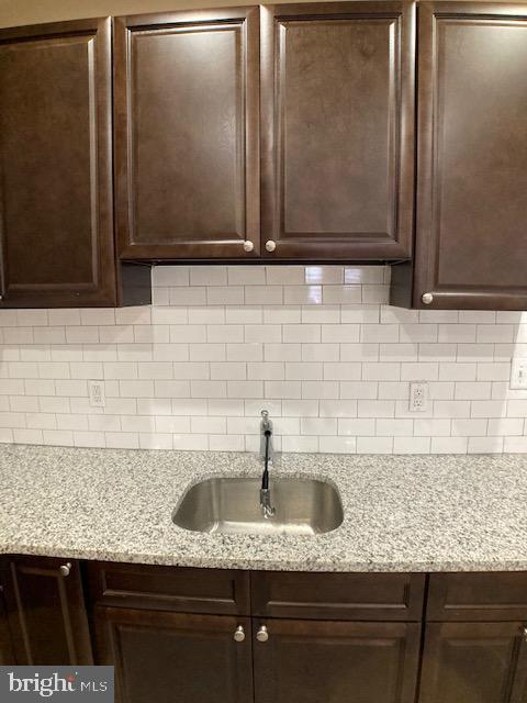 kitchen with dark brown cabinets, light stone counters, a sink, and tasteful backsplash