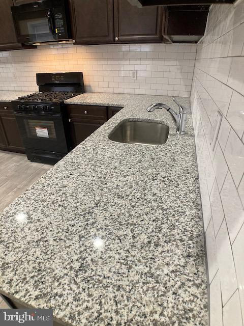 kitchen featuring dark brown cabinetry, tasteful backsplash, light stone countertops, black appliances, and a sink