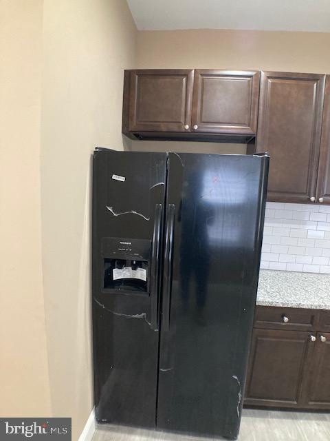 kitchen with dark brown cabinetry, light stone counters, black refrigerator with ice dispenser, and backsplash