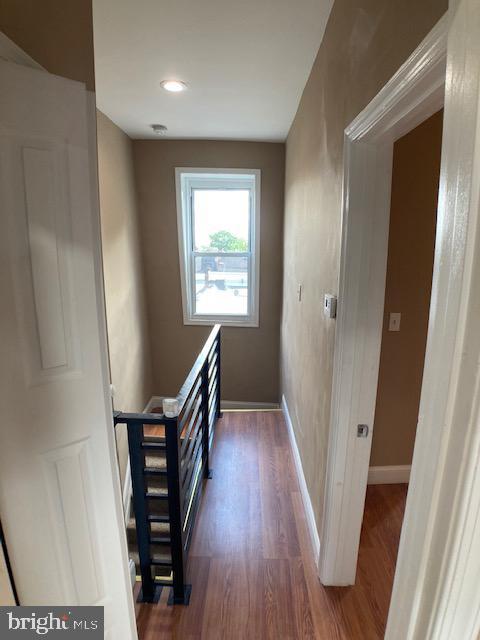 corridor with dark wood-style floors, baseboards, and an upstairs landing