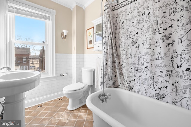 full bathroom with toilet, ornamental molding, tile patterned flooring, a freestanding bath, and tile walls