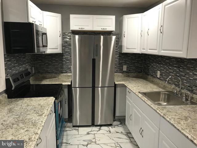 kitchen featuring marble finish floor, stainless steel appliances, a sink, and white cabinetry