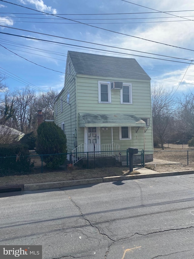 traditional-style home featuring a fenced front yard, an AC wall unit, and roof with shingles