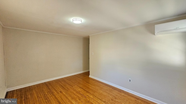 spare room with ornamental molding, a wall mounted AC, wood finished floors, and baseboards