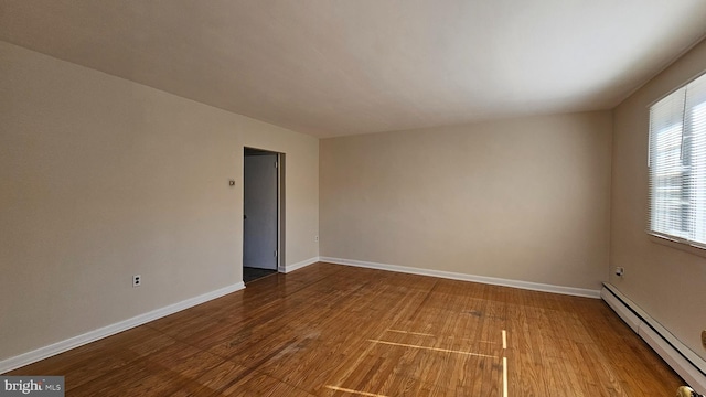 unfurnished room with a baseboard heating unit, baseboards, and wood finished floors