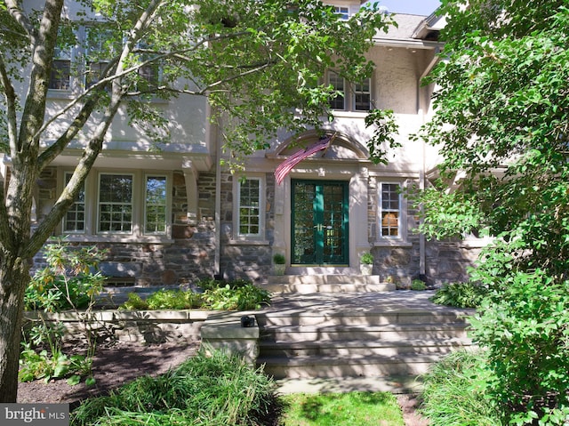 view of front facade featuring entry steps, stone siding, and stucco siding