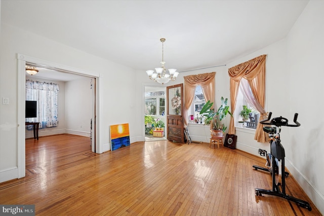 workout area featuring a notable chandelier, baseboards, and light wood finished floors