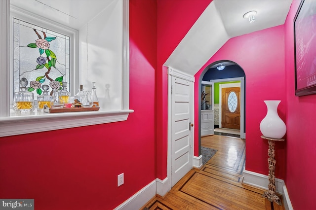 hallway featuring baseboards, plenty of natural light, wood finished floors, and vaulted ceiling