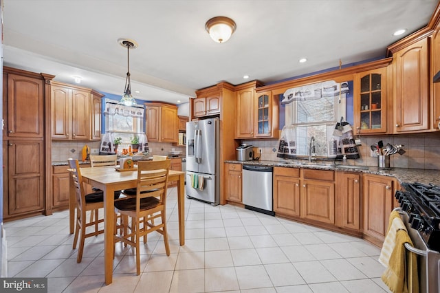 kitchen featuring glass insert cabinets, decorative light fixtures, stone countertops, stainless steel appliances, and a sink