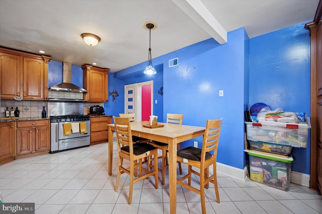 kitchen featuring backsplash, brown cabinetry, wall chimney range hood, decorative light fixtures, and stainless steel gas stove