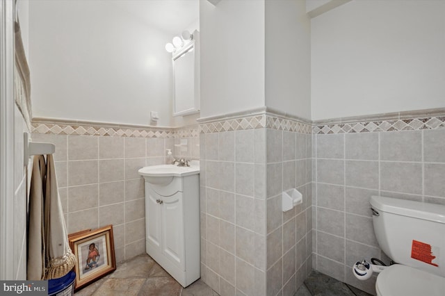 half bathroom with vanity, tile walls, toilet, and wainscoting