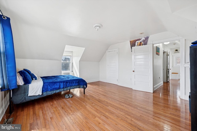 bedroom with baseboards, lofted ceiling, and hardwood / wood-style flooring