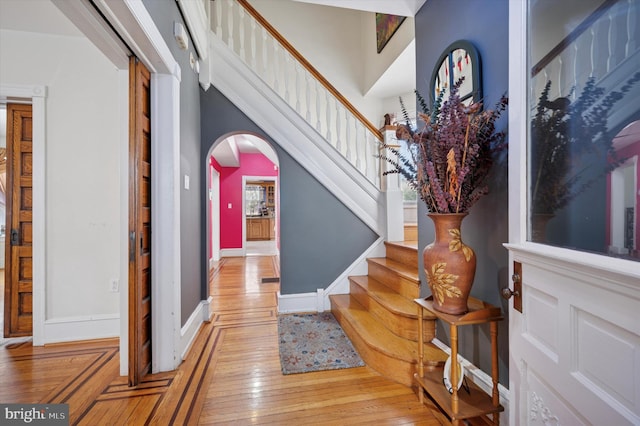 foyer entrance with arched walkways, light wood-style flooring, stairs, and baseboards