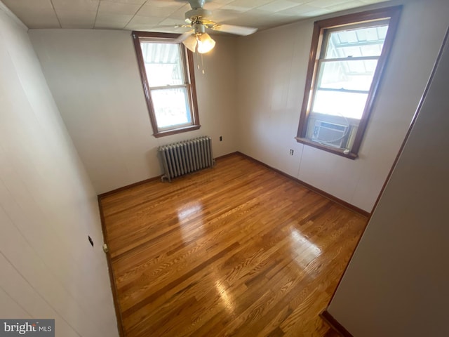 spare room with cooling unit, radiator heating unit, a ceiling fan, and wood finished floors