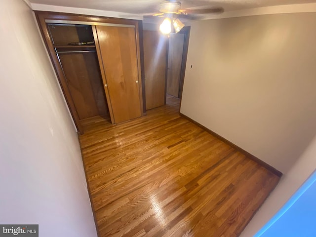 unfurnished bedroom featuring a ceiling fan, light wood-style flooring, baseboards, and a closet