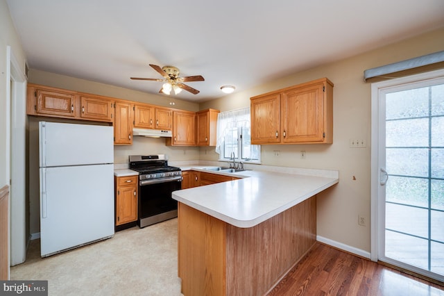 kitchen featuring stainless steel range with gas stovetop, freestanding refrigerator, a peninsula, light countertops, and a sink