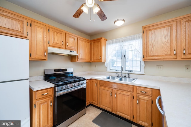 kitchen featuring light countertops, freestanding refrigerator, a sink, stainless steel gas range, and under cabinet range hood