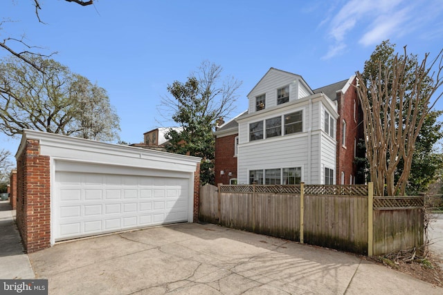view of property exterior with fence, brick siding, an outbuilding, and a detached garage