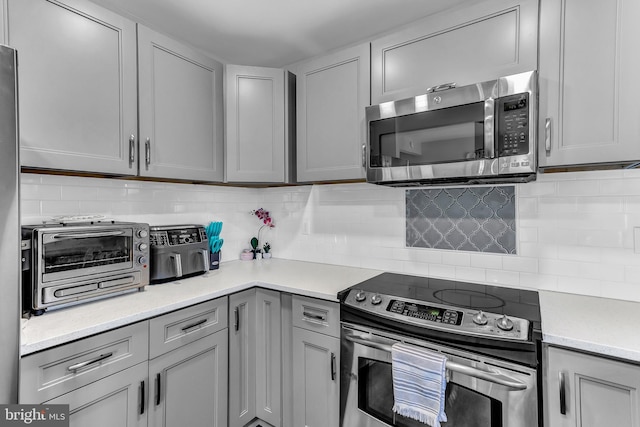 kitchen featuring a toaster, decorative backsplash, stainless steel appliances, light countertops, and gray cabinetry