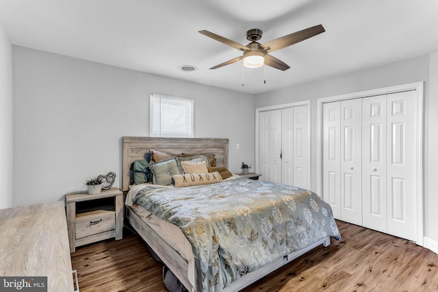 bedroom with a ceiling fan, wood finished floors, visible vents, and multiple closets