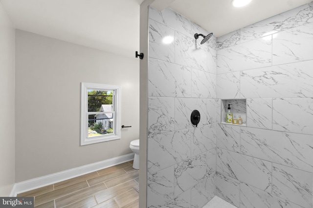 bathroom with wood tiled floor, a tile shower, toilet, and baseboards