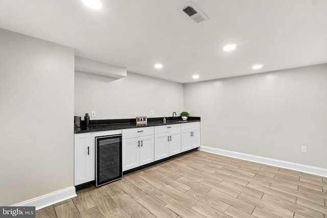 kitchen featuring light wood finished floors, beverage cooler, visible vents, white cabinets, and a sink