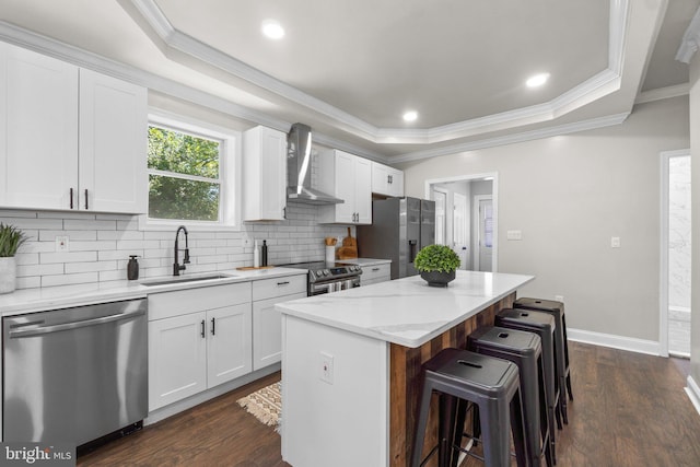 kitchen featuring stainless steel appliances, white cabinets, a sink, a kitchen island, and wall chimney exhaust hood