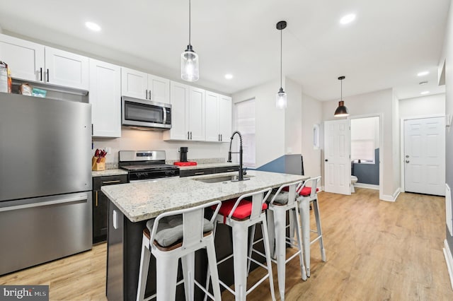 kitchen with a sink, light stone countertops, appliances with stainless steel finishes, light wood-style floors, and a kitchen island with sink