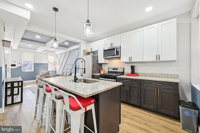 kitchen featuring light wood finished floors, coffered ceiling, a center island with sink, and appliances with stainless steel finishes