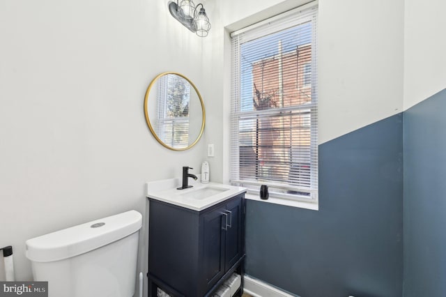 half bath featuring baseboards, toilet, and vanity