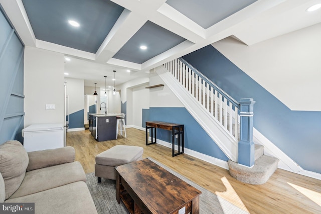 living room featuring stairs, light wood-style flooring, baseboards, and coffered ceiling