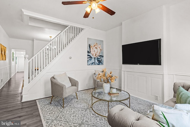 living room featuring a wainscoted wall, a decorative wall, a ceiling fan, wood finished floors, and stairs