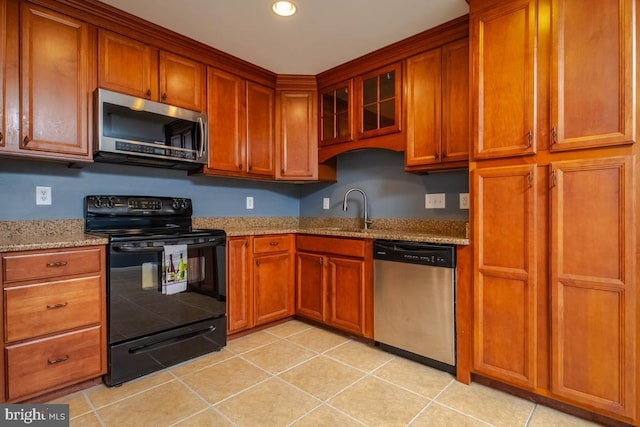 kitchen with appliances with stainless steel finishes, brown cabinetry, a sink, and light stone countertops