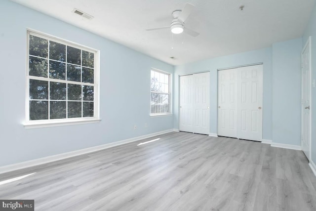 unfurnished bedroom with multiple closets, visible vents, baseboards, and wood finished floors